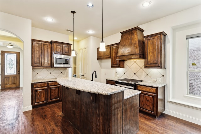 kitchen featuring pendant lighting, custom exhaust hood, appliances with stainless steel finishes, and dark hardwood / wood-style floors