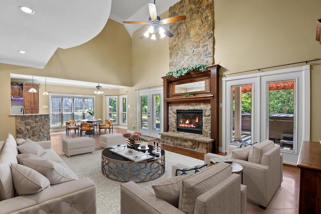 living room with ceiling fan, a stone fireplace, light wood-type flooring, and high vaulted ceiling