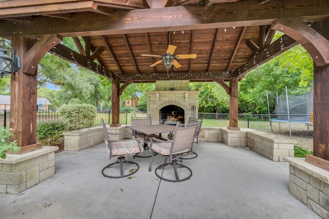 view of patio / terrace featuring a trampoline, an outdoor stone fireplace, a gazebo, and ceiling fan