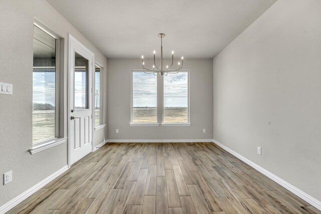 unfurnished dining area with an inviting chandelier, a healthy amount of sunlight, and light hardwood / wood-style floors