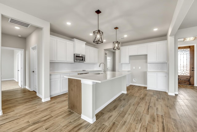 kitchen featuring white cabinets, decorative light fixtures, sink, backsplash, and a center island with sink