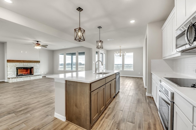 kitchen with white cabinetry, a center island with sink, appliances with stainless steel finishes, light wood-type flooring, and sink