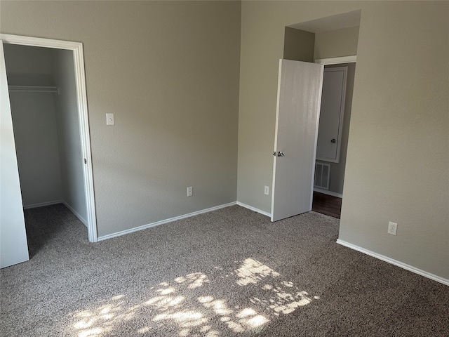 unfurnished bedroom featuring a closet, dark colored carpet, and a spacious closet