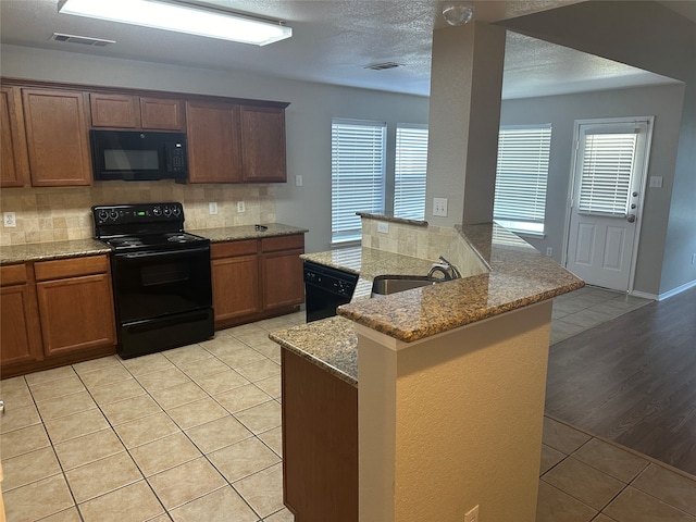 kitchen with light stone counters, tasteful backsplash, light wood-type flooring, black appliances, and sink