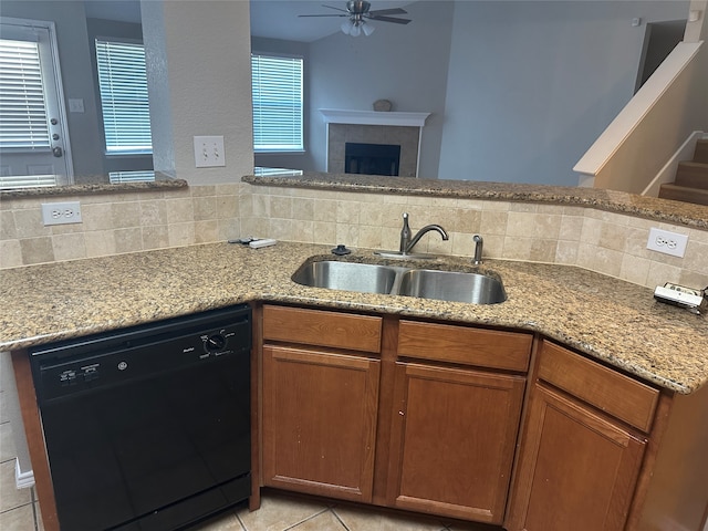 kitchen featuring a fireplace, dishwasher, sink, and light stone counters