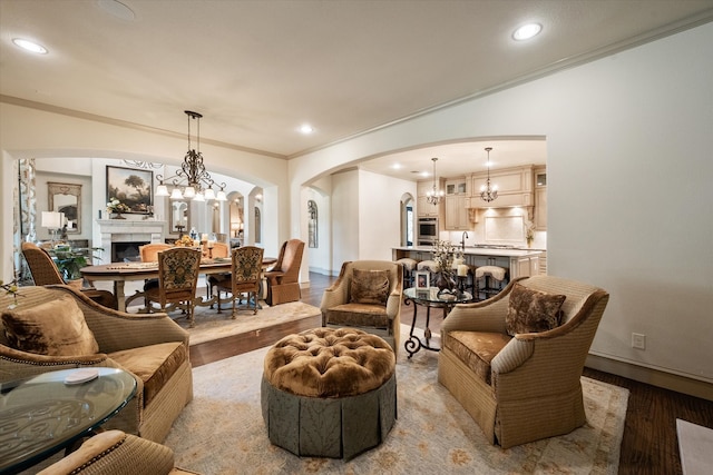 living room with light wood-type flooring, a tile fireplace, crown molding, and a notable chandelier