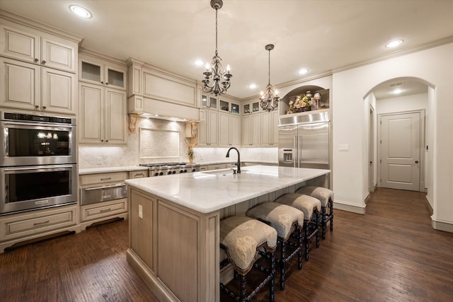 kitchen featuring dark wood-type flooring, sink, an island with sink, appliances with stainless steel finishes, and decorative light fixtures