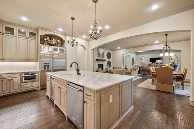 kitchen with decorative light fixtures, a center island with sink, dark wood-type flooring, appliances with stainless steel finishes, and a fireplace