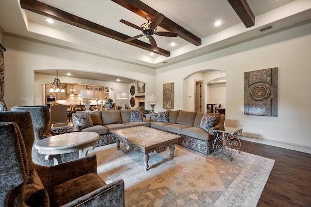 living room featuring ceiling fan with notable chandelier, beamed ceiling, and dark hardwood / wood-style floors