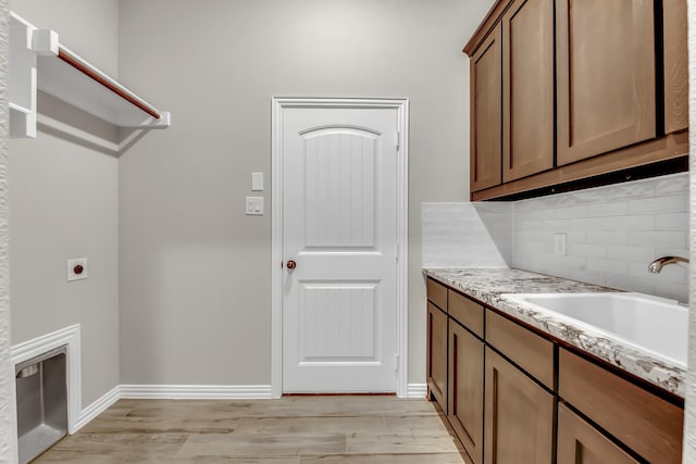 clothes washing area with cabinets, light hardwood / wood-style floors, electric dryer hookup, and sink