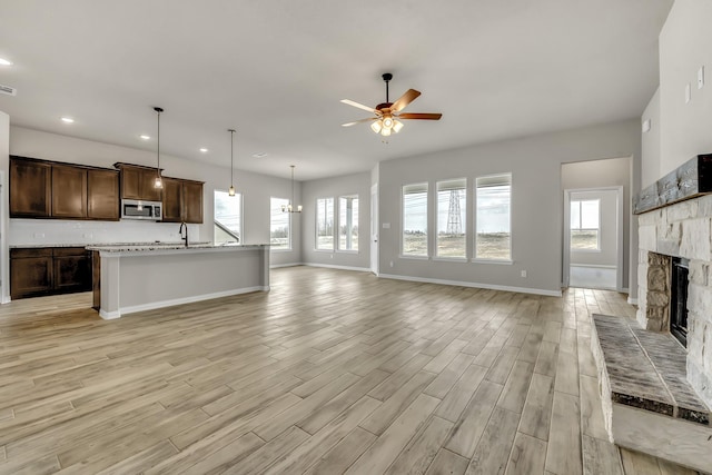 unfurnished living room with ceiling fan with notable chandelier, a fireplace, and sink