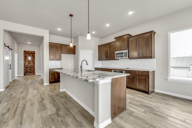 kitchen with light stone countertops, an island with sink, sink, light hardwood / wood-style flooring, and a barn door