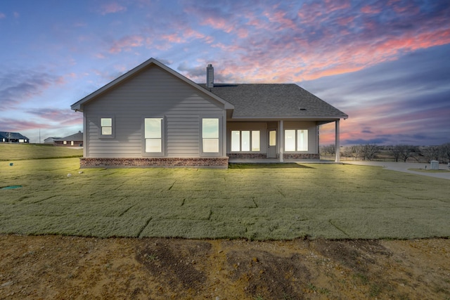 back house at dusk featuring a lawn