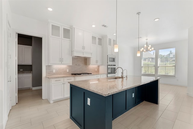 kitchen featuring light stone countertops, white cabinets, sink, a chandelier, and a center island with sink