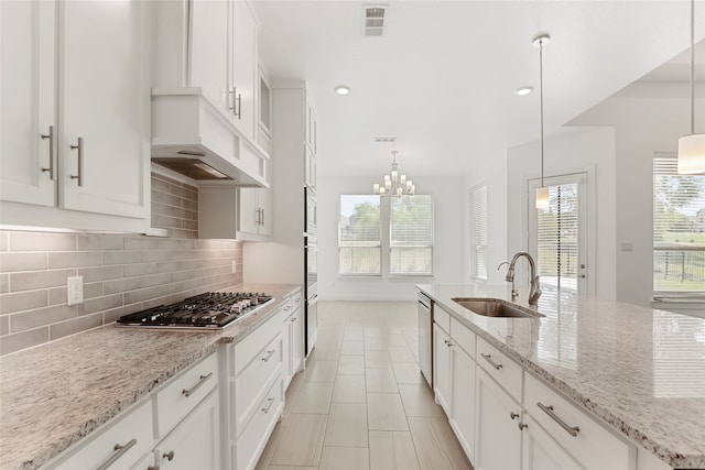 kitchen with light stone counters, white cabinets, sink, decorative light fixtures, and appliances with stainless steel finishes