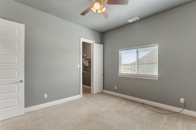 unfurnished bedroom featuring light carpet, a spacious closet, ceiling fan, and a closet