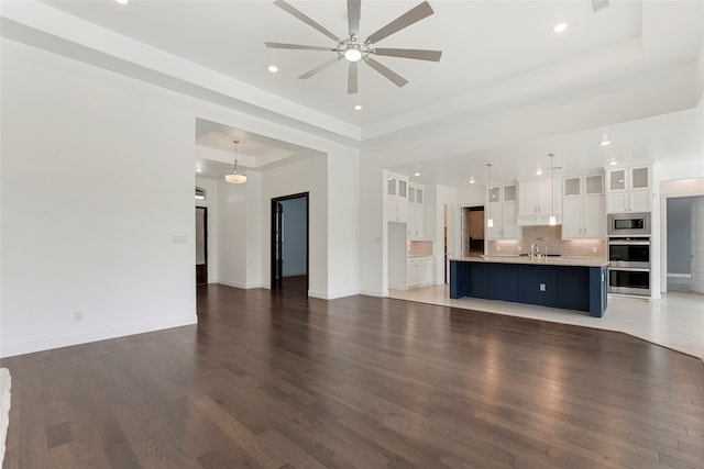 unfurnished living room featuring ceiling fan, sink, a raised ceiling, and dark wood-type flooring