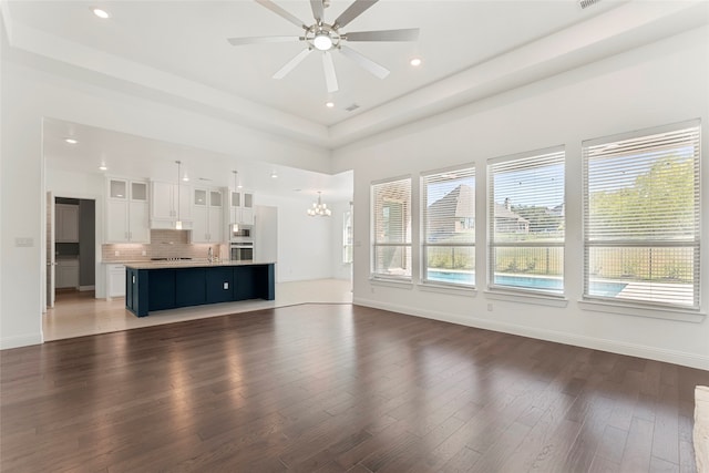 unfurnished living room with ceiling fan with notable chandelier, dark hardwood / wood-style floors, and a wealth of natural light