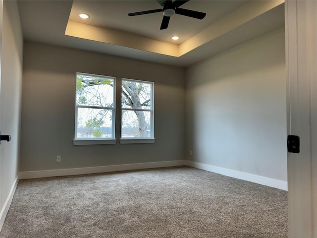 unfurnished room with a raised ceiling, ceiling fan, and carpet