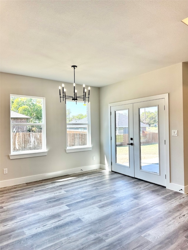 unfurnished dining area featuring a textured ceiling, wood-type flooring, a chandelier, and french doors