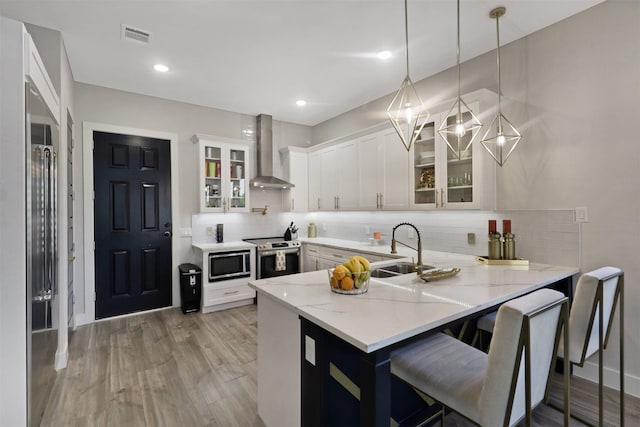 kitchen featuring white cabinets, wall chimney exhaust hood, pendant lighting, and kitchen peninsula