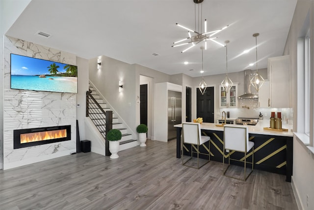 kitchen with wood-type flooring, a breakfast bar area, white cabinets, hanging light fixtures, and wall chimney exhaust hood