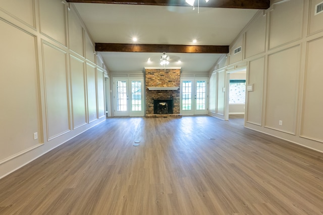 unfurnished living room featuring ceiling fan, a fireplace, lofted ceiling with beams, french doors, and light wood-type flooring