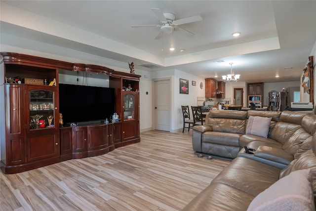 living room featuring ceiling fan with notable chandelier, a tray ceiling, and light hardwood / wood-style flooring