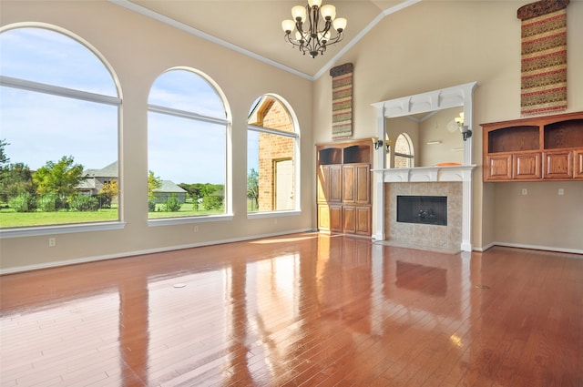 unfurnished living room with high vaulted ceiling, a tiled fireplace, an inviting chandelier, light hardwood / wood-style flooring, and ornamental molding