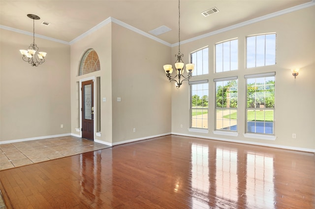 unfurnished room with an inviting chandelier, a towering ceiling, hardwood / wood-style flooring, and ornamental molding