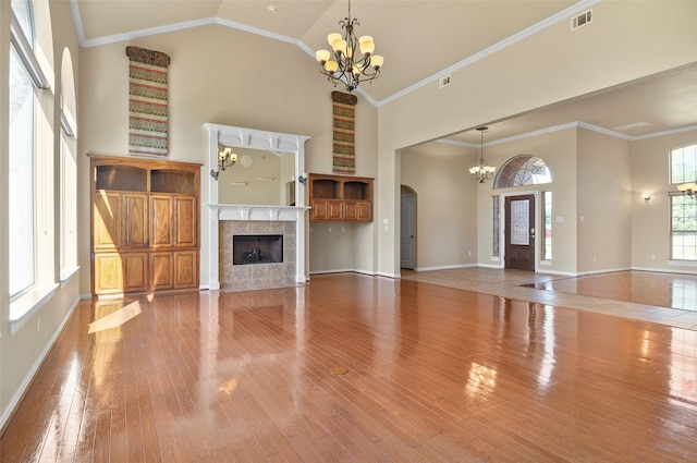 unfurnished living room featuring high vaulted ceiling, ornamental molding, a tiled fireplace, and hardwood / wood-style floors