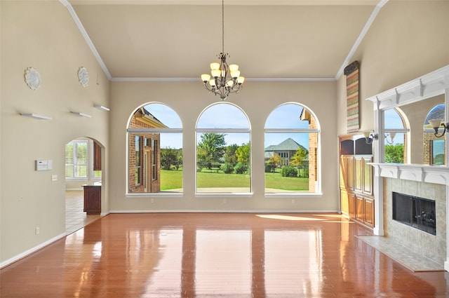 unfurnished living room with a tiled fireplace, light hardwood / wood-style flooring, an inviting chandelier, crown molding, and a high ceiling