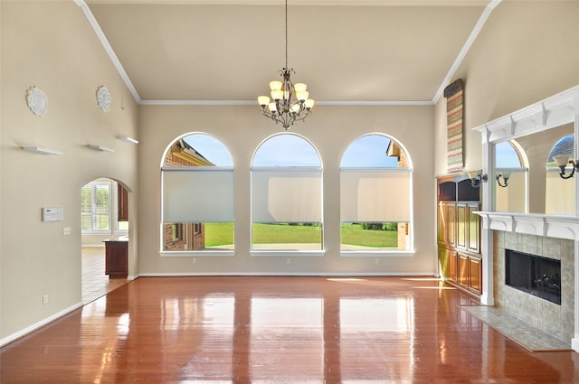 unfurnished living room featuring a high ceiling, a chandelier, a tile fireplace, and hardwood / wood-style floors