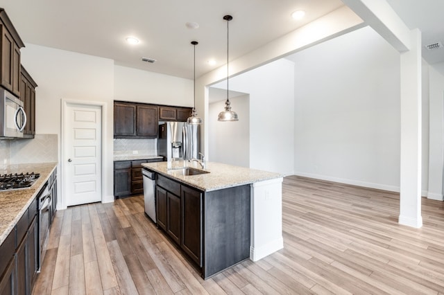 kitchen featuring an island with sink, decorative light fixtures, stainless steel appliances, light wood-type flooring, and decorative backsplash