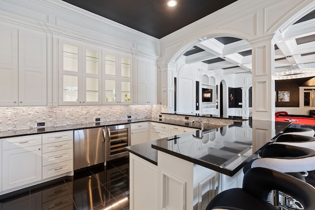 kitchen featuring a kitchen breakfast bar, decorative columns, beverage cooler, coffered ceiling, and white cabinets