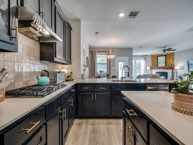 kitchen featuring light hardwood / wood-style floors, sink, appliances with stainless steel finishes, decorative light fixtures, and a large fireplace