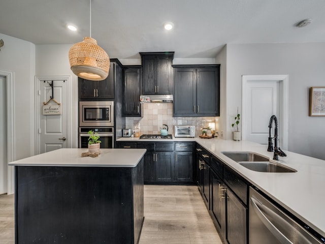 kitchen with light wood-type flooring, sink, hanging light fixtures, decorative backsplash, and appliances with stainless steel finishes