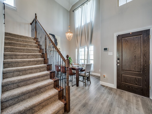 entryway featuring an inviting chandelier, a towering ceiling, a wealth of natural light, and light wood-type flooring