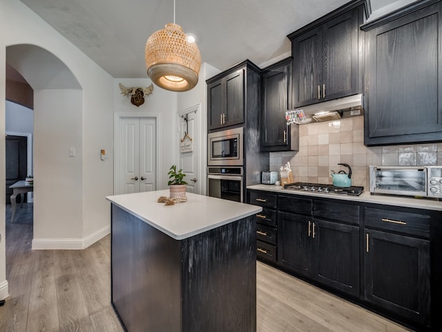 kitchen featuring pendant lighting, light hardwood / wood-style flooring, backsplash, appliances with stainless steel finishes, and a center island