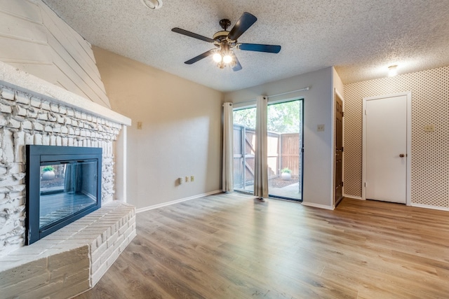 unfurnished living room with a fireplace, ceiling fan, light hardwood / wood-style flooring, and a textured ceiling