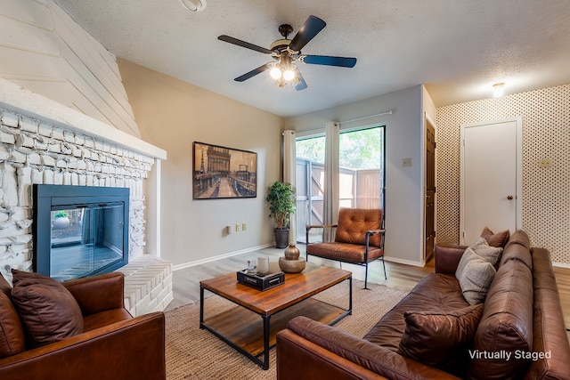 living room with a brick fireplace, a textured ceiling, light hardwood / wood-style floors, and ceiling fan