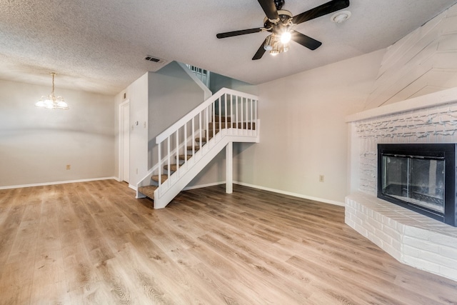 unfurnished living room with wood-type flooring, ceiling fan with notable chandelier, a textured ceiling, and a fireplace