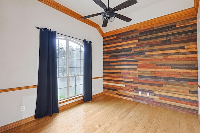 empty room with wood walls, ceiling fan, light wood-type flooring, and crown molding