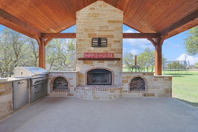 view of patio / terrace featuring grilling area, a trampoline, exterior kitchen, and an outdoor stone fireplace