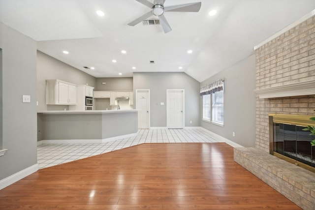 unfurnished living room with a fireplace, light hardwood / wood-style floors, vaulted ceiling, and ceiling fan