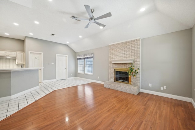 unfurnished living room featuring a brick fireplace, a textured ceiling, vaulted ceiling, ceiling fan, and light hardwood / wood-style floors