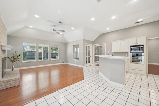 kitchen with lofted ceiling, a kitchen island with sink, ceiling fan, white cabinetry, and stainless steel appliances