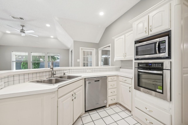 kitchen with lofted ceiling, sink, appliances with stainless steel finishes, white cabinetry, and kitchen peninsula