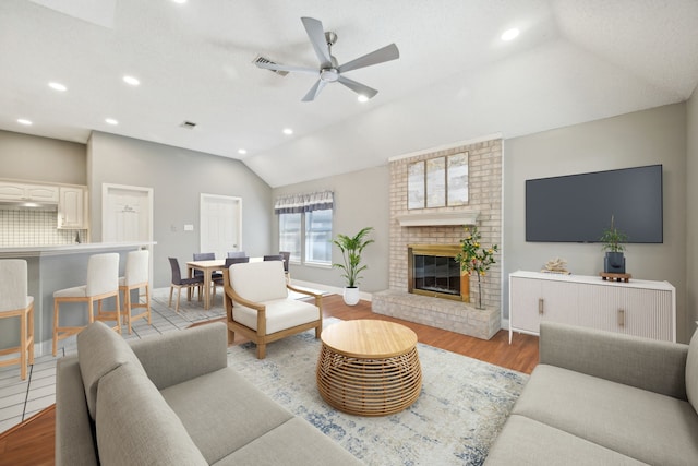 living room with a fireplace, light hardwood / wood-style floors, vaulted ceiling, and ceiling fan