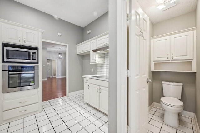 kitchen with decorative backsplash, a textured ceiling, stainless steel appliances, white cabinets, and light tile patterned flooring